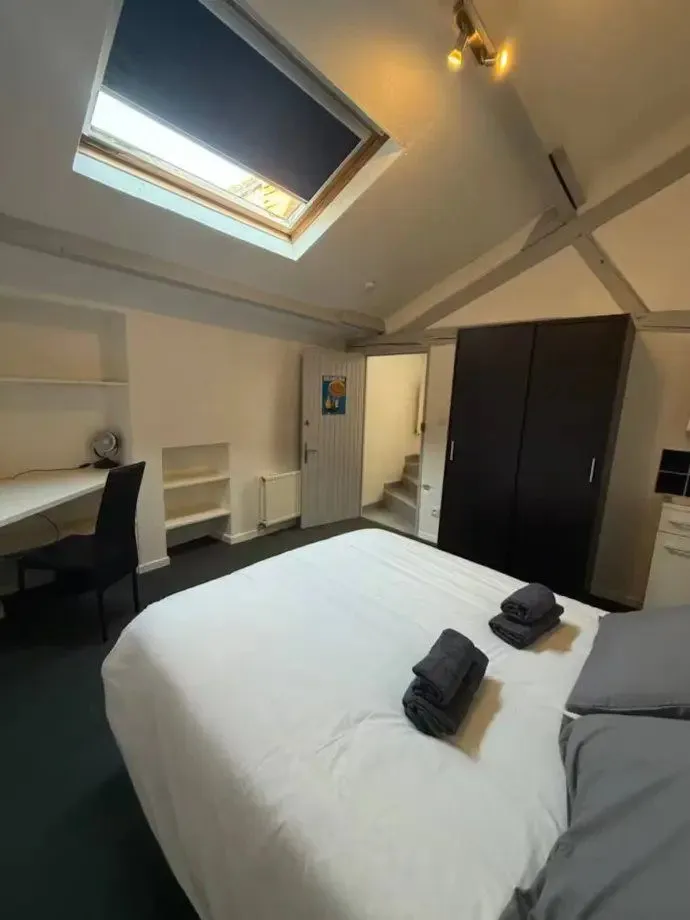 Chambre aménagée dans les combles, fenêtre de toit au-dessus du lit, bureau contre le mur.