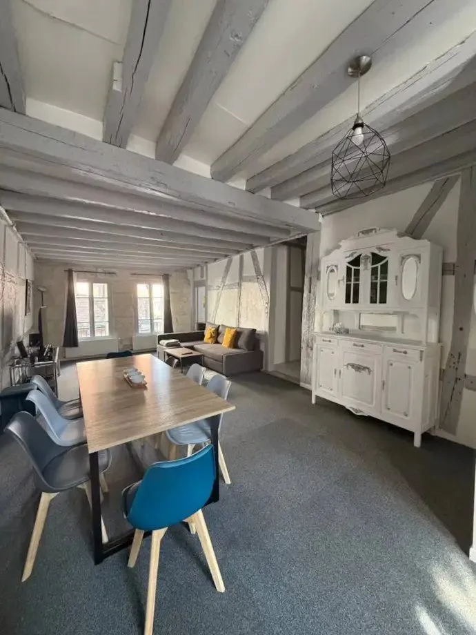Salle à manger sous colombages apparents, table en bois clair et chaises dépareillées.