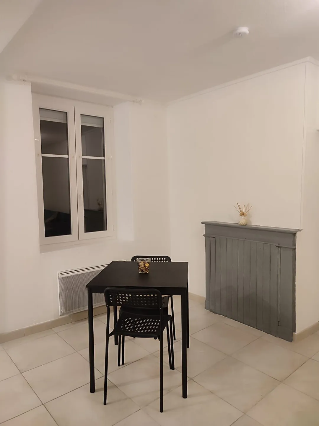 Coin repas : table noire et chaises devant un buffet gris, sol carrelé clair.