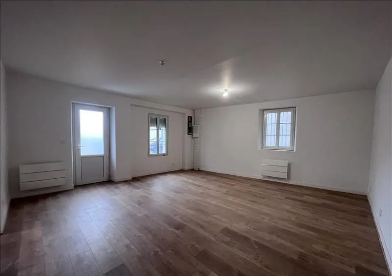 Le salon refait : murs blancs, sol stratifié et deux fenêtres.