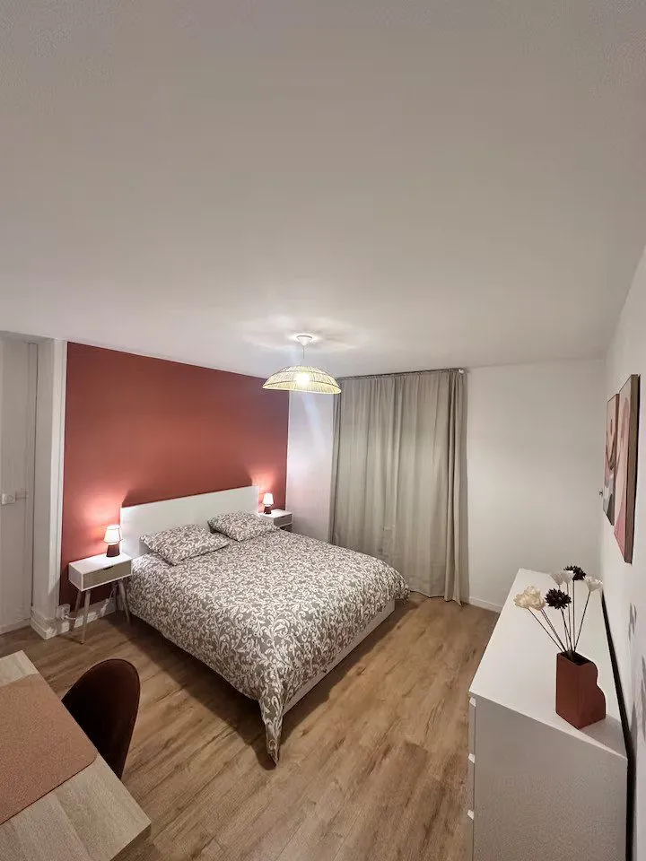 Chambre avec mur terracotta, lit double et parquet clair.