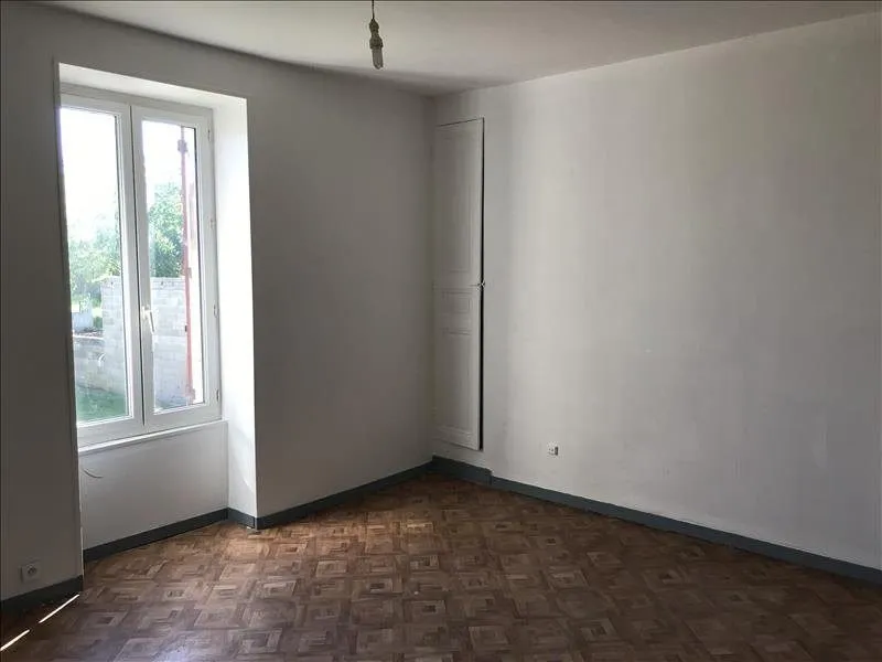 Pièce vide au parquet ancien, murs blancs et fenêtre à deux battants.
