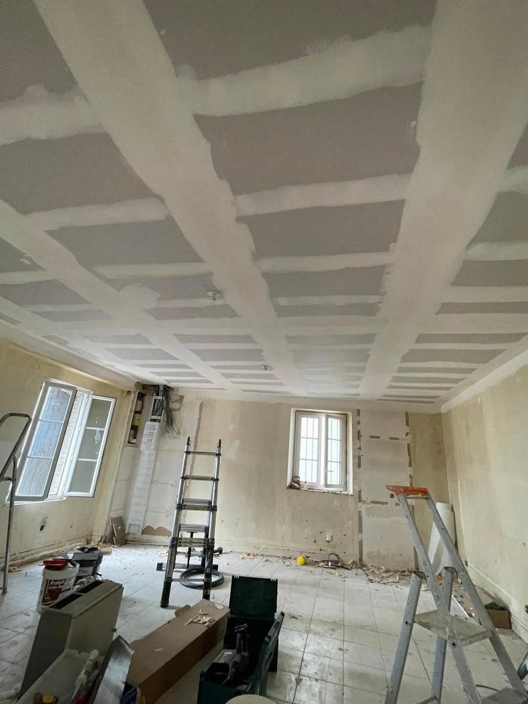Plafond refait en plaques de plâtre, escabeau et matériel au sol.