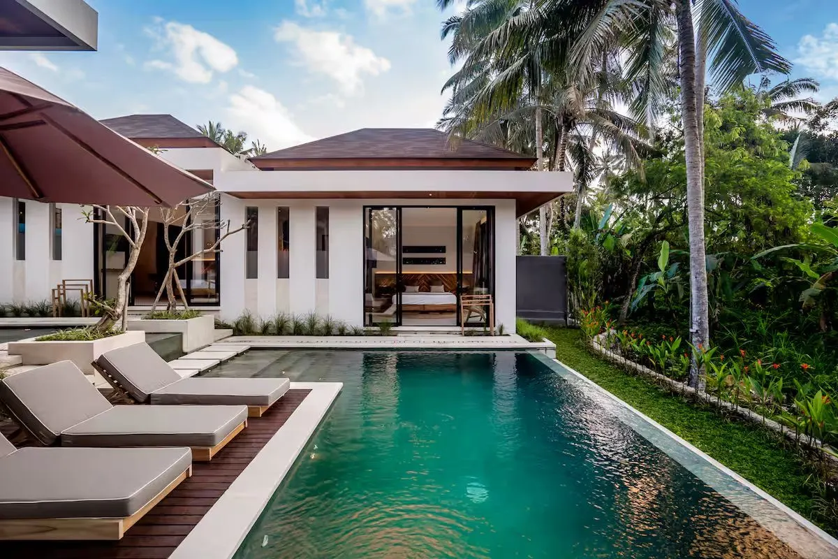 La villa vue depuis la piscine : toiture basse, baies vitrées et transats sur la terrasse en bois.